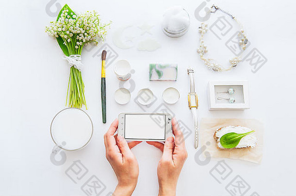 美博客概念女手保持智能手机背景风格绿色植物白色详细一些配件白色工作场所