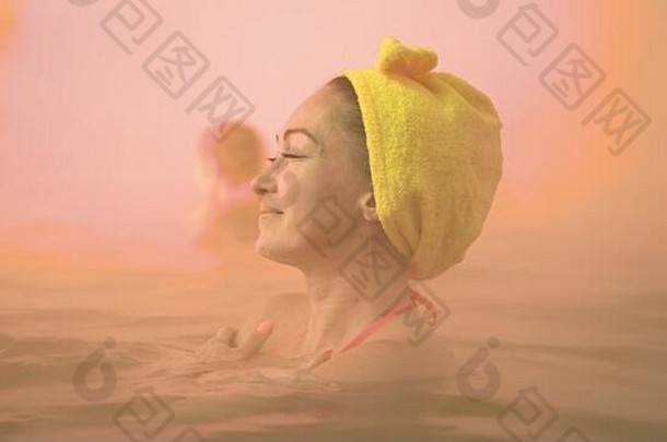 特写镜头：一名白人妇女在传统的户外温泉浴场游泳，沐浴在温暖的盐水中，沐浴着柔和的神奇粉色灯光蒸汽。地热温泉。