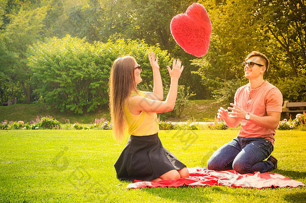 爱情和约会。年轻时尚的情侣们在公园里和大红心玩得很开心。野餐的概念。