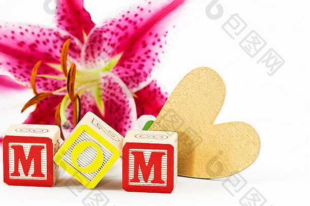 在白色背景下，一朵百合花映衬着金色的心形和字母大写字母拼写“妈妈”。