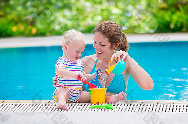 幸福的家庭，年轻活泼的母亲和可爱的<strong>小卷发</strong>宝宝在游泳池里玩耍，玩玩具浇水