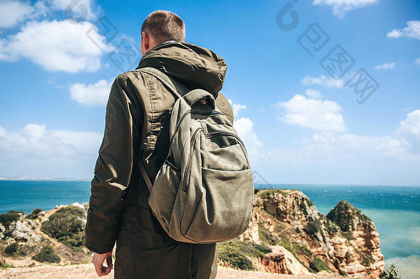 一位背着背包的游客或旅行者沿着大西洋海岸散步，欣赏葡萄牙拉各斯市附近美丽的海洋景色。