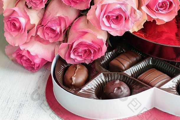 十几朵柔软的长茎粉色<strong>玫瑰</strong>花，木质背景上有一盒心形巧克力糖，是情人节礼物。