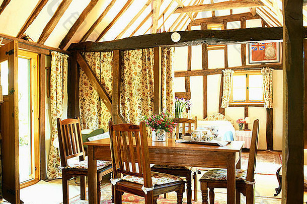 有横梁的乡村餐厅里有古色古香的桌椅，顶部天花板和厚重的<strong>窗帘</strong>向后拉，以展示入口大厅
