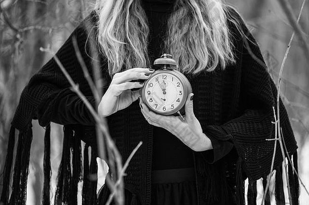 一张妇女手持复古时钟的特写照片，显示时间为5到12点。