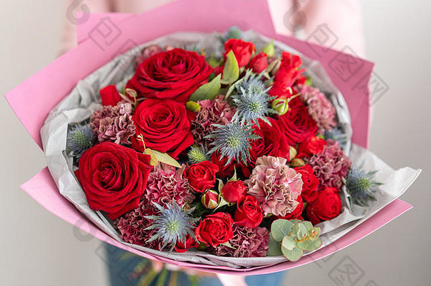 混合的红色调的花束。一束美丽的鲜花在女人的手中。花店花匠的工作。鲜切花。