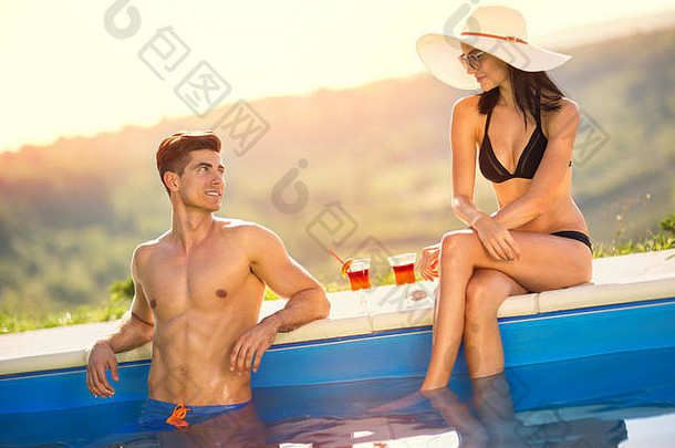 这对年轻夫妇在游泳池里尽情享受，喝着鸡尾酒