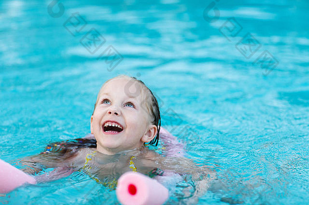暑假时，可爱的小女孩在游泳池里拿着粉色泡面游泳