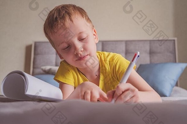 年轻的白人男孩坐在家里的床上<strong>画册</strong>，在纸上写字。
