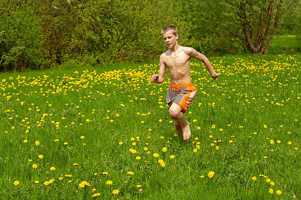 一个十几岁的男孩光着脚跑过一个长满蒲公英的花园。