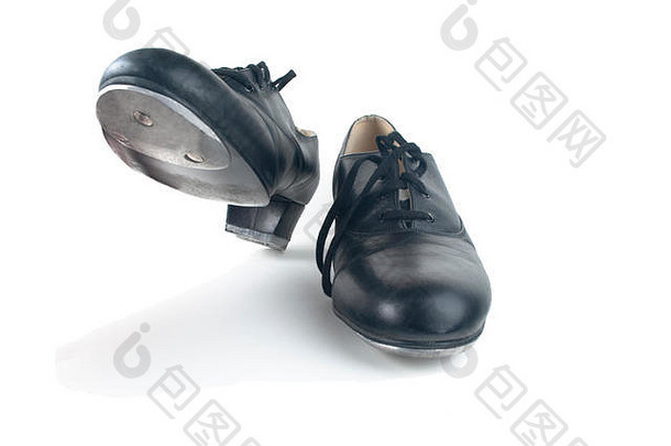 一双用过的带鞋带的黑色踢踏鞋，一双放在地上，一双抬起，随时准备踏上。白色背景，阴影可见。