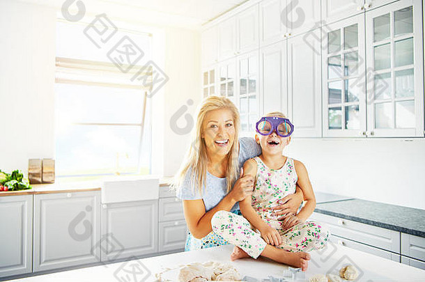 明亮的厨房场景，一位女士坐在桌子上，戴着愚蠢的紫色眼镜抱着笑孩子