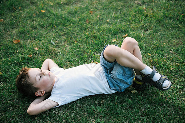 在纽约中央公园，一个可爱的小男孩躺在落叶丛中的绿草上