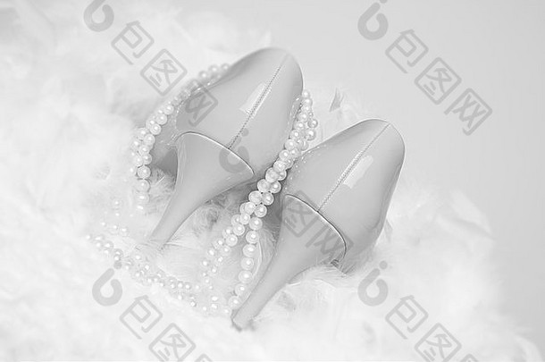 白色毛皮和羽毛上有一双白色漆皮鞋；一只鞋的侧面挂着珍珠