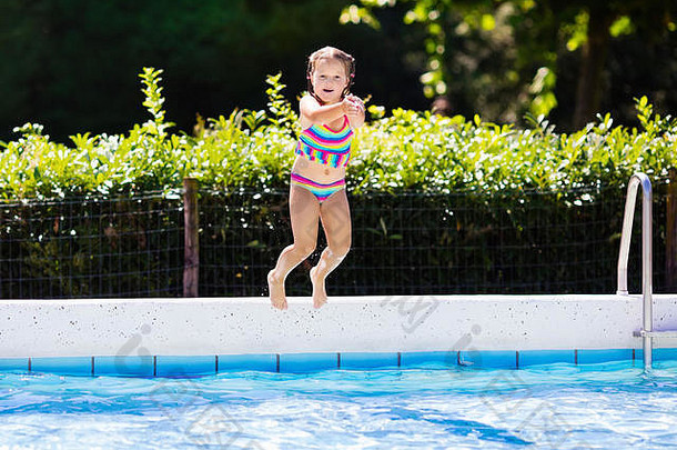 家庭暑假期间，一个快乐的小女孩跳进了热带度假胜地的室外游泳池。孩子们学习游泳。