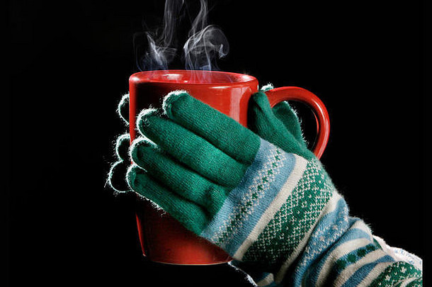 在寒冷的日子里，手套手拿着热气腾腾的饮料。黑色孤立