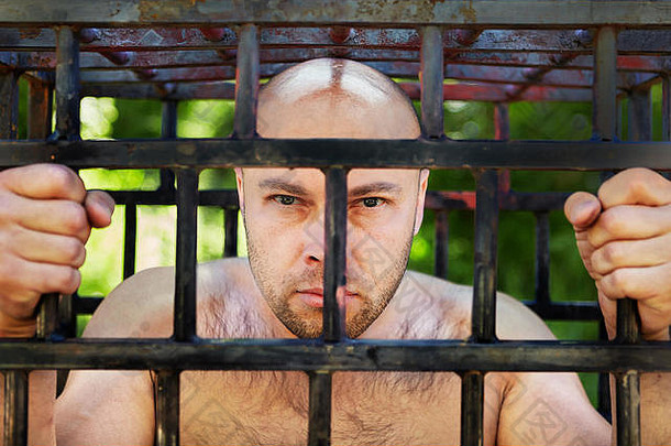 一个秃头男人从牢房后面看去，他因绑架、逮捕、拘留的司法判决或判刑而被监禁。