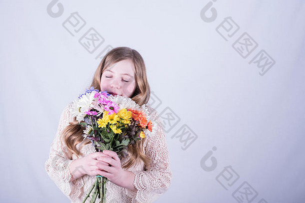 微笑着的12岁女孩，一头又长又脏的金发，手上拿着一束五颜六色的雏菊，眼睛紧闭在白色背景下