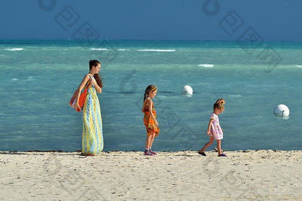夏天假期妈妈。可爱的女儿走桑迪海滩蓝色的海洋背景古巴卡亚椰子树