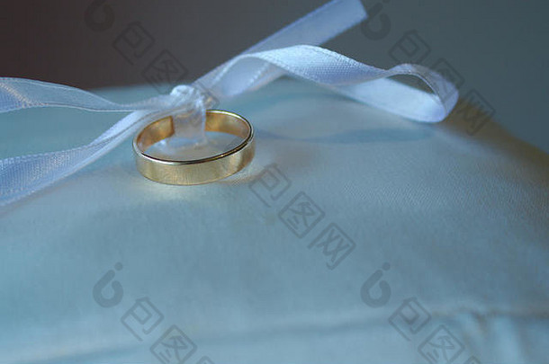 一条绑在蝴蝶结上的白丝带把结婚戒指放在枕头上。