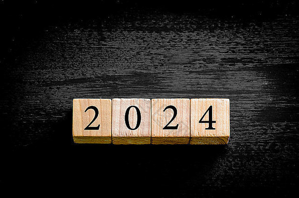 <strong>2024</strong>年。木制小立方体，数字在黑色背景上隔离，并留有复印空间。<strong>新年</strong>概念图。