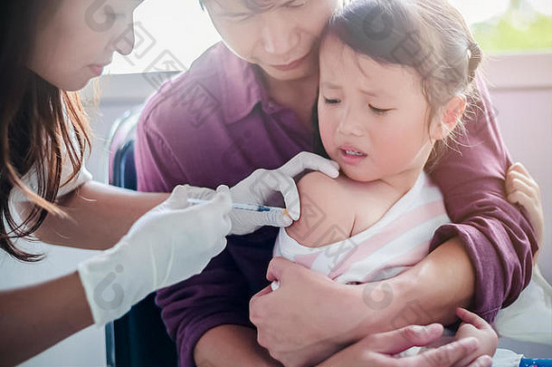 正在打针的小孩，特写医生给亚洲小女孩的手臂打针，和父亲拥抱孩子，为了不扭动一会儿
