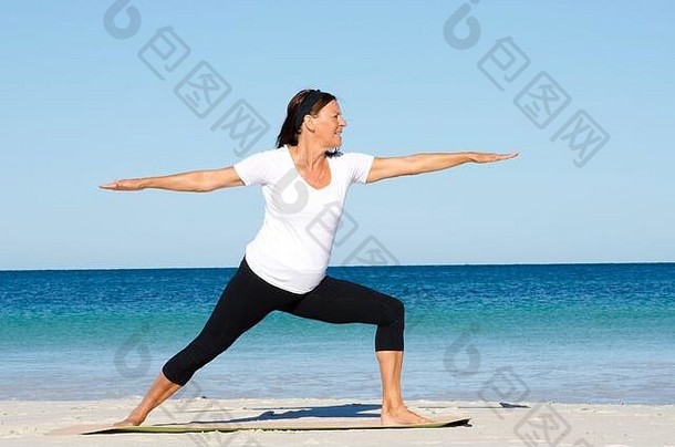 有吸引力的活跃的高级女人保持适合健康的伸展运动普拉提练习海滩海洋蓝色的天空背景复制