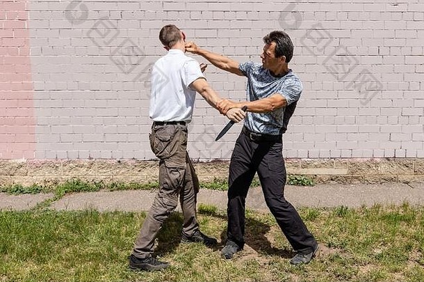 成熟的男教练用刀攻击者的脸。街头斗殴。克拉夫·马加的自卫技术