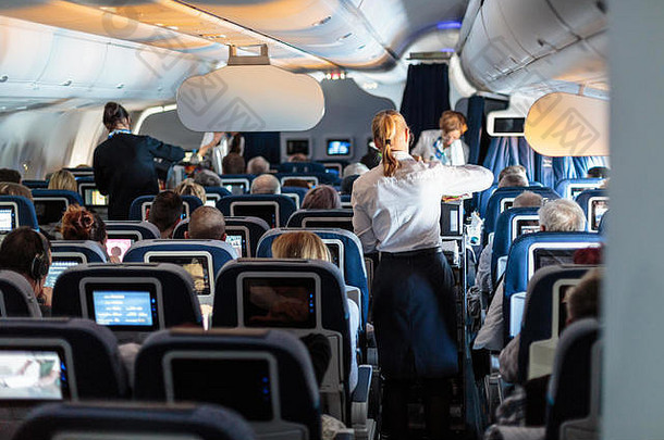 大型商用飞机的内部，飞行中有空姐在座位上为乘客服务。