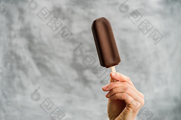 一名手持爱斯基摩派冰淇淋的妇女，背景为灰色。爱斯基摩派日概念