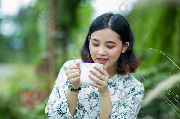 年轻的亚洲女孩喜欢在花园里喝咖啡