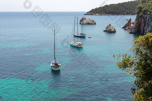 在<strong>希腊</strong>斯科佩洛斯，一个有悬崖和清澈海水的<strong>希腊</strong>岛屿的海湾视图，背景是几艘游艇。