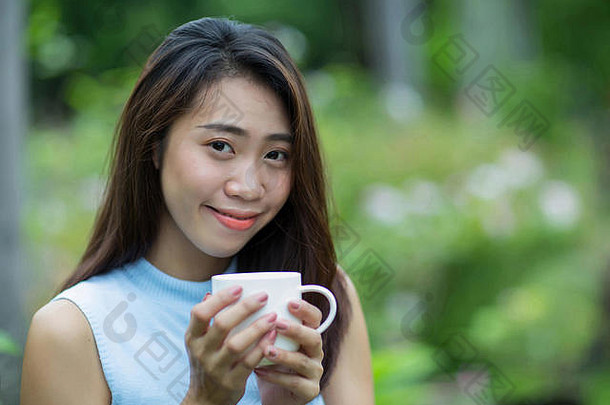 年轻的亚洲女孩持有杯咖啡花园