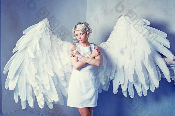 美丽的年轻模特穿着白色连衣裙，在工作室里有天使的翅膀