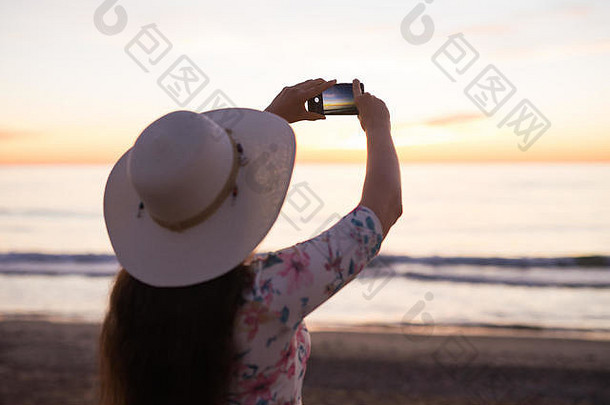 年轻女子在度假旅行时，用<strong>手机</strong>或智能<strong>手机数码</strong>相机拍摄大海和日落，并将其上传到网上。