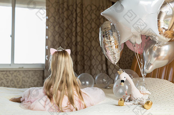 室内拍摄的是一个非常快乐的金发小女孩，她用气球庆祝6岁生日，穿着时装，非常兴奋