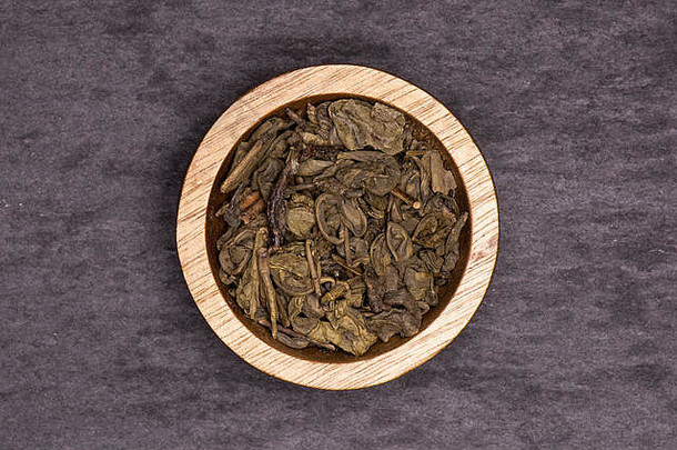 许多干绿茶，木制碗平放在灰色石头上