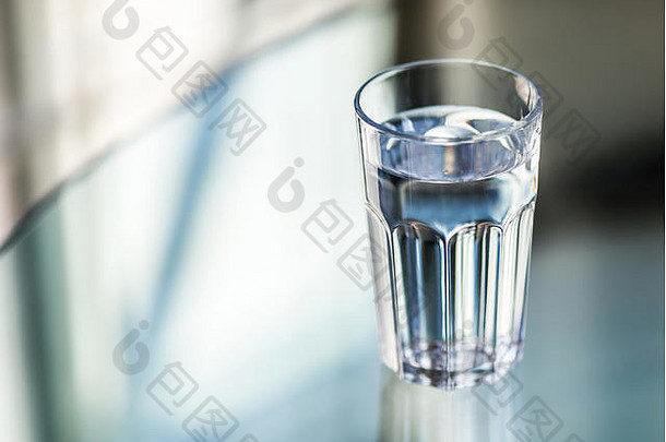 背景模糊的玻璃桌上放着一杯水