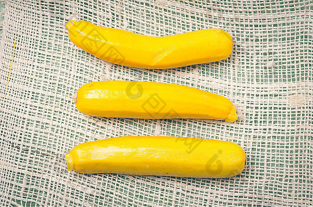 三个新鲜的有机黄色西葫芦在布上