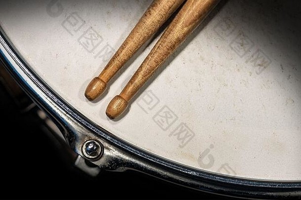 两个木制鼓槌的特写镜头，背景为深色的旧金属圈套鼓。打击乐器