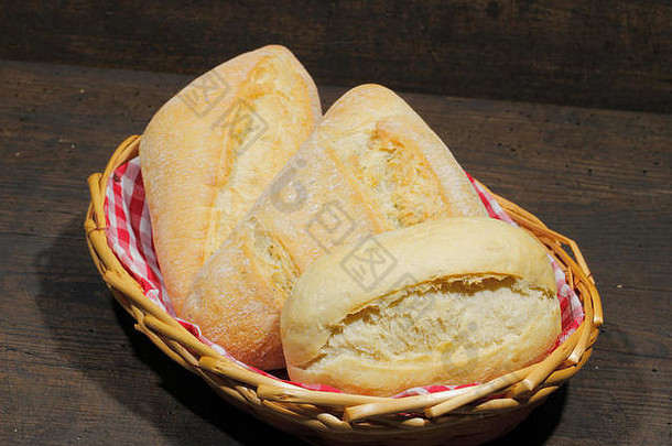 各种类型的面包卷、蛋糕、小面包，放在一个篮子里，放在一个质朴的木制表面上