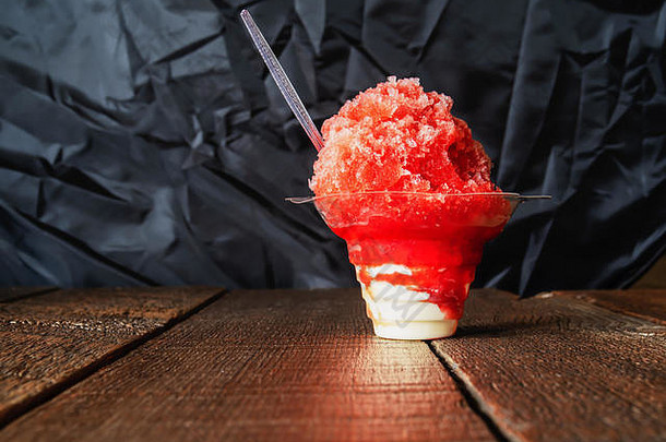 红色刨冰、刨冰或雪糕放在透明杯中的香草冰淇淋上，木质背景，留有复印空间。