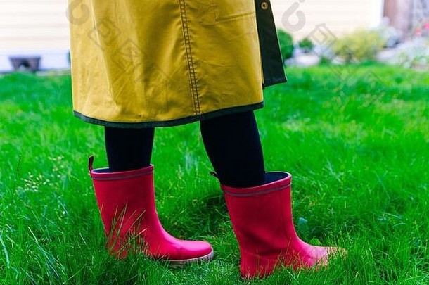 黄色雨衣。粉色橡胶靴，防雨淋。绿色草地上穿着靴子的腿的概念图。