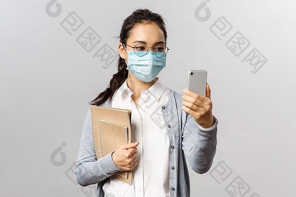病毒、健康和医学概念。年轻的亚洲女孩戴着医用面具，拿着笔记本和工作报告，在智能手机上自拍