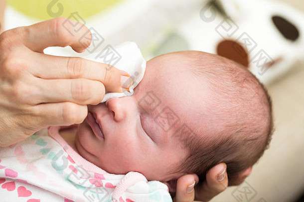 母亲用棉条上的生理溶液清洁新生儿的眼睛