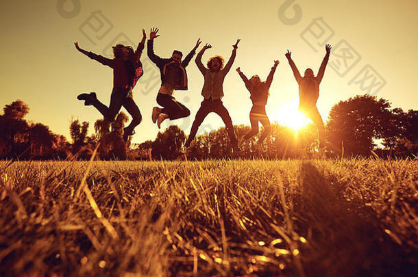 日落时一群年轻人在公园的草地上跳跃。