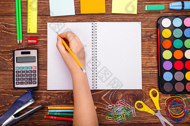 打开空白笔记本，手拿毛笔，在木制书桌的背景上放着一个学校用品的框架。将拷贝空间返回到sch