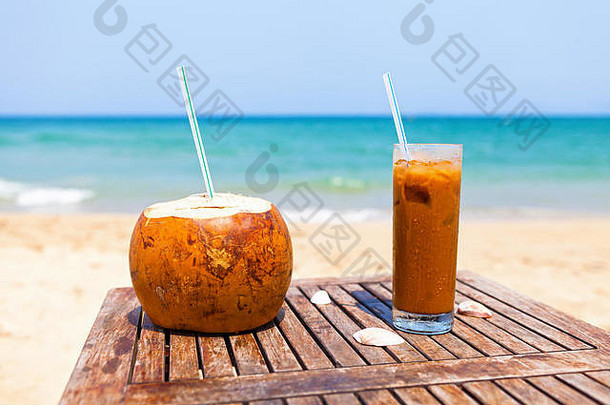 椰子<strong>饮料</strong>和冰咖啡放在木桌上，映衬着美丽的海滩和翠绿的大海