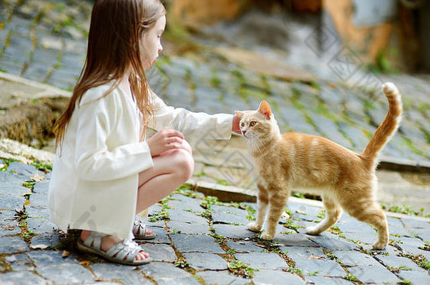 可爱的小女孩在典型的意大利小镇的狭窄街道上散步时遇到了一只猫