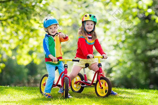 孩子们骑平衡自行车。孩子们在阳光公园骑自行车。在温暖的夏日，小女孩和男孩骑着滑翔机自行车。学龄前儿童学习平衡